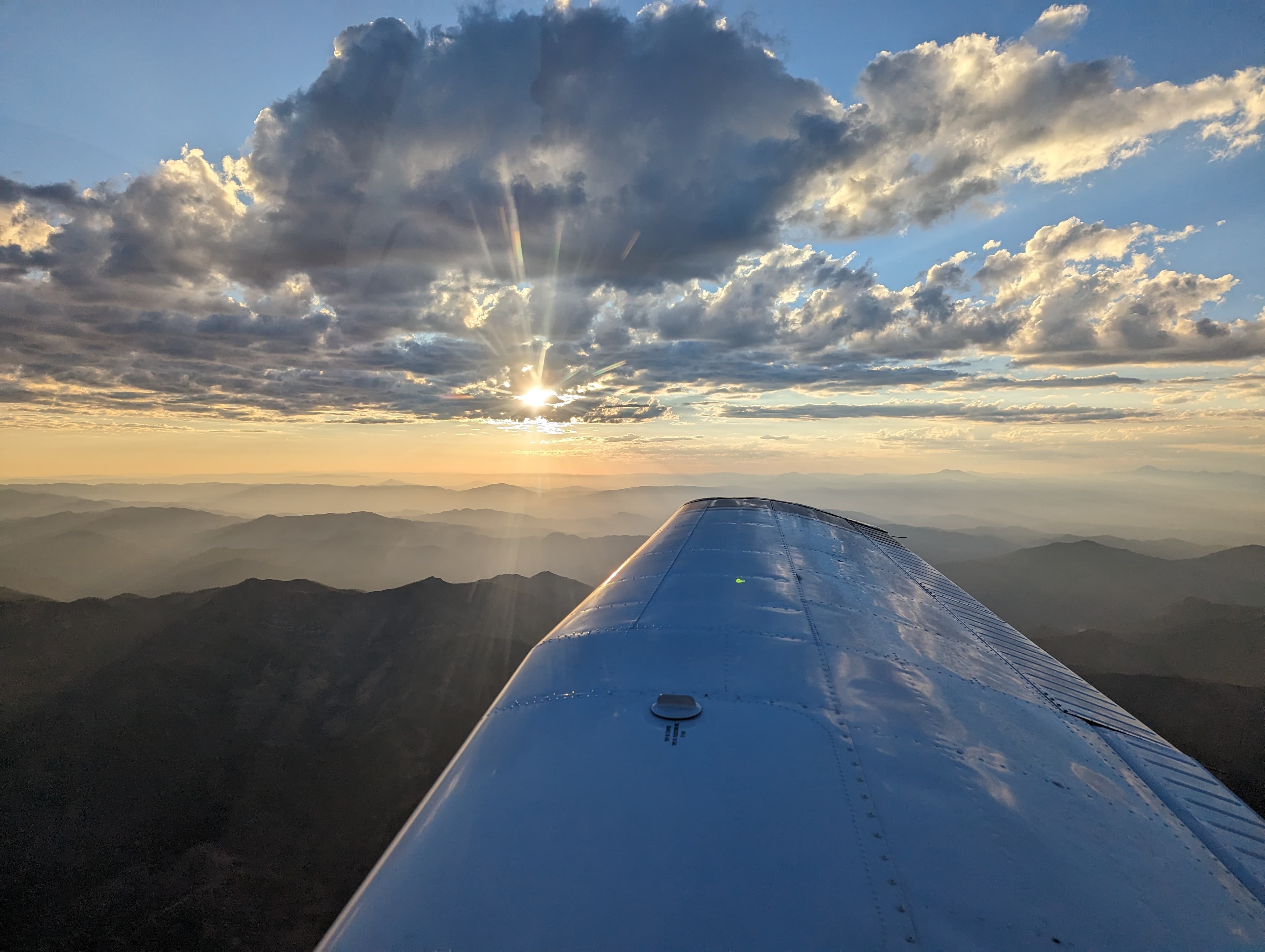 Sunset over layered mountains and the wing of a light aircraft